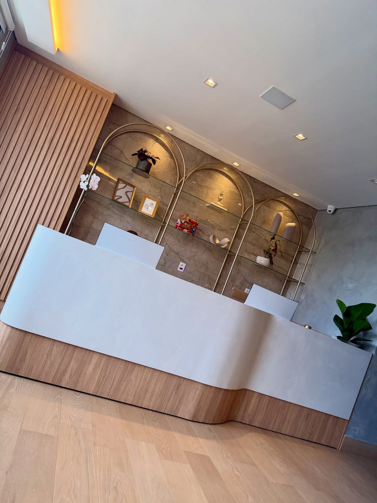 Recepção comercial com balcão branco curvo e estante em arcos dourados